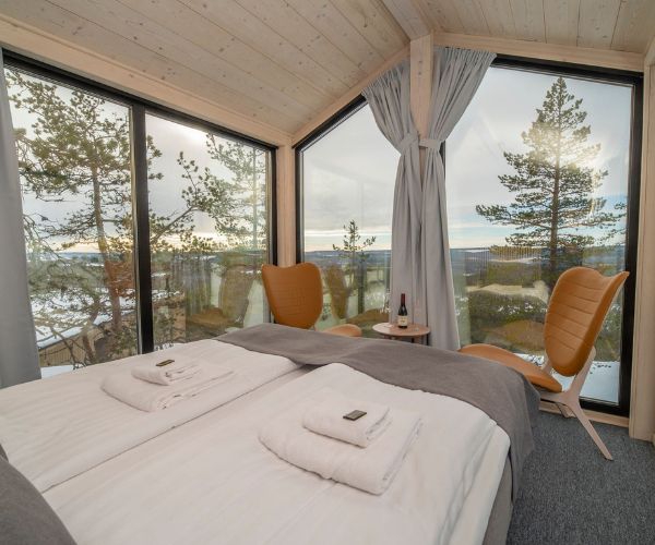 Chambre lumineuse d’une tiny house en bois Doxar avec vue panoramique sur la forêt enneigée