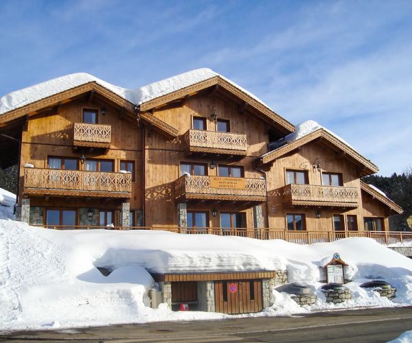 Complexe de chalets en bois à Méribel sous la neige, façade principale avec trois pignons et balcons sculptés.