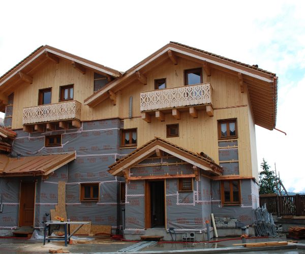 Façade de chalet en bois en cours de chantier avec pare-pluie et menuiseries posées.