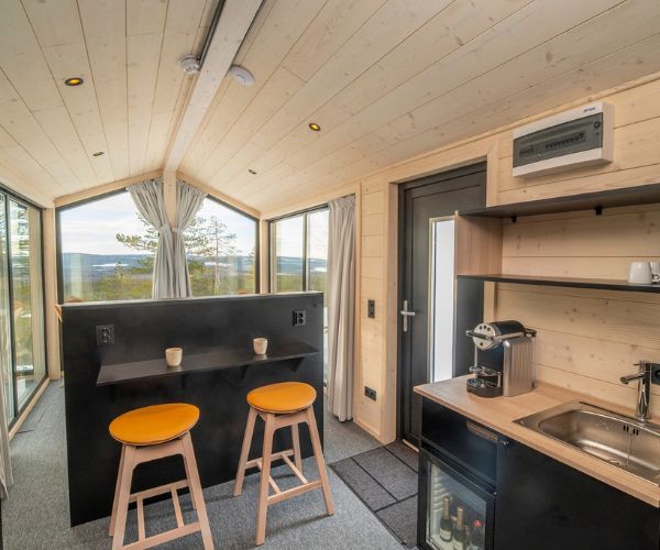 Intérieur d’une tiny house en bois Doxar avec coin cuisine et bar face aux grandes baies vitrées.