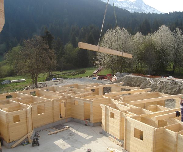 Montage des murs en bois d’un complexe touristique, grue soulevant une poutre.