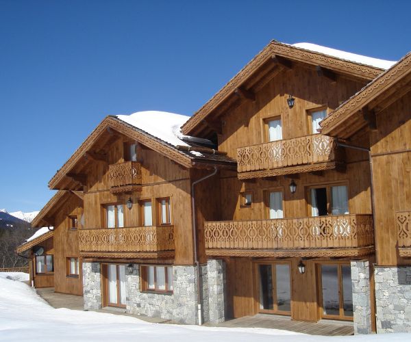 Chalets en bois achevés à Méribel sous ciel bleu, balcons décoratifs et pierre en soubassement.